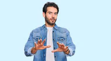 Günlük giysiler giyen genç İspanyol adam korku ifadesinden korkuyor ve dehşete düşüyor. El hareketlerini durdur, şok içinde bağır. panik konsepti. 