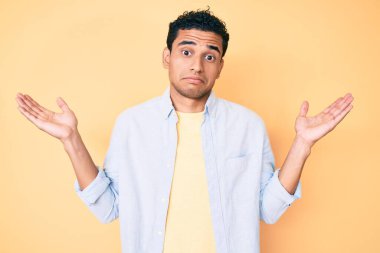 Sarı arka planda dikilen yakışıklı İspanyol genç adam habersiz ve kolları açık, hiçbir fikri yok ve şüpheli bir yüzü var.. 