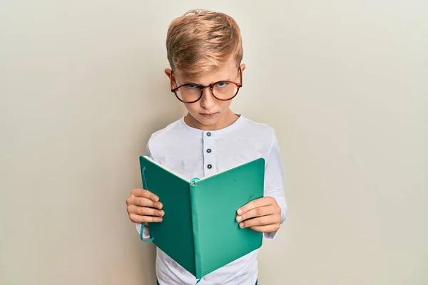 小さな白人の少年が眼鏡をかけて本を読んで懐疑的で緊張し 問題のために動揺して眉をひそめています 否定的な人 — ストック写真
