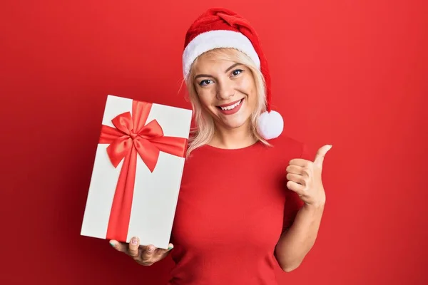 Jovem Loira Vestindo Chapéu Natal Segurando Presente Sorrindo Feliz Positivo — Fotografia de Stock