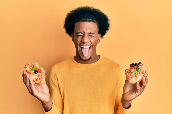 Hombre Afroamericano Con Cabello Afro Sosteniendo Pasteles Dulces Sacando Lengua — Foto de Stock