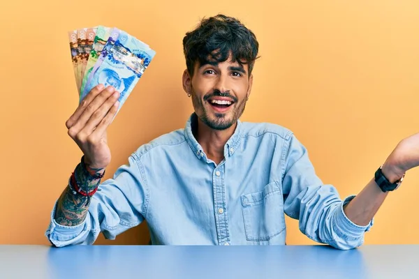 Joven Hispano Sosteniendo Dólares Australianos Sentado Mesa Celebrando Logro Con —  Fotos de Stock