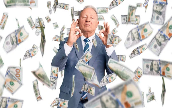 Kıdemli yakışıklı, gri saçlı, şık takım elbiseli, rahat ve gülümseyen, gözleri kapalı, parmaklarıyla meditasyon hareketi yapan adam. yoga konsepti.