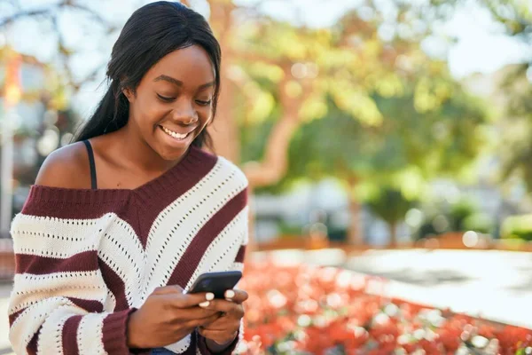 若いアフリカ系アメリカ人の女性が公園でスマートフォンを使って笑顔で幸せ — ストック写真