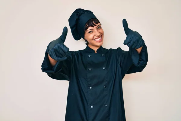 漂亮的黑发女人穿着职业厨师制服 肯定用手做积极的手势 微笑着竖起大拇指 为成功感到高兴 优胜手势 — 图库照片