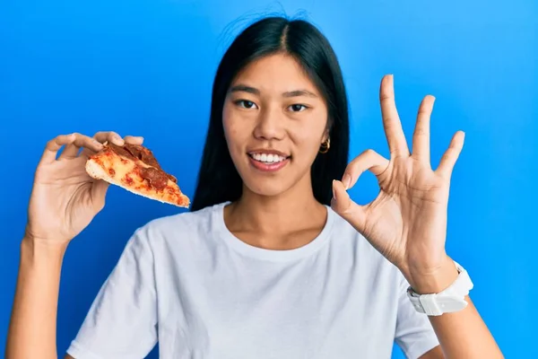 Młoda Chinka Jedząca Smaczną Pizzę Pepperoni Robi Znak Palcami Uśmiechając — Zdjęcie stockowe