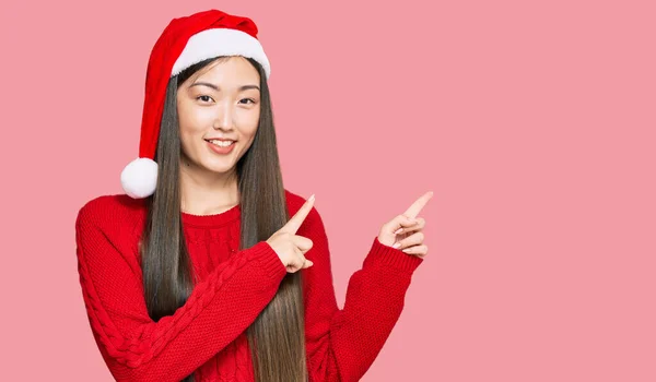 若いです中国人女性身に着けていますクリスマスの帽子笑顔と見てカメラを指しています二つの手と指で側面 — ストック写真