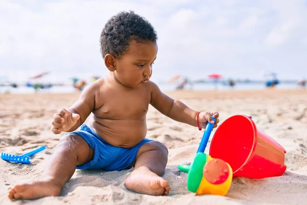 愛らしいアフリカ系アメリカ人の幼児はおもちゃで遊んでいます砂の上に座ってビーチ — ストック写真