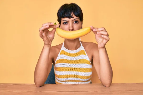 問題のために動揺を眉をひそめて 面白い笑顔懐疑的かつ神経のようなバナナを保持ブルネットのティーンエイジャーの女の子 否定的な人 — ストック写真