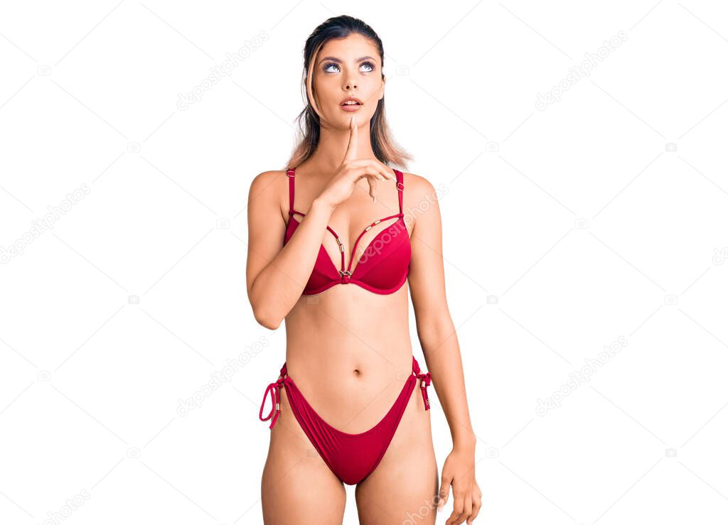 Young beautiful woman wearing bikini thinking concentrated about doubt with finger on chin and looking up wondering 