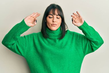 Günlük kazak giyen genç İspanyol kadın rahatla ve gülümse gözleri kapalı parmaklarıyla meditasyon hareketi yapıyor. yoga konsepti. 