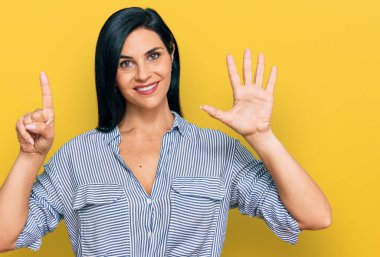 Gündelik giysiler giyen genç beyaz kadın altı numarayı gösterip işaret ederken kendinden emin ve mutlu gülümsüyor.. 