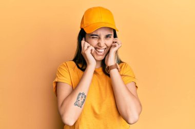 Dağıtım üniforması giyen ve yüksek sesli müzik sesi için kulaklarını parmaklarıyla kapatan Latin kökenli genç bir kadın. sağır kavramı. 