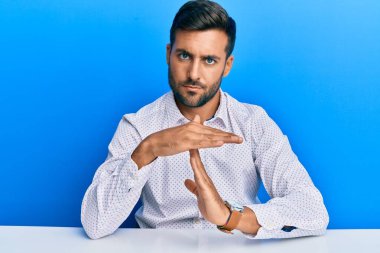 İş kıyafetleri giymiş yakışıklı İspanyol bir adam masada oturuyor. El kol hareketleri yapıyor, hayal kırıklığına uğramış ve ciddi bir yüz ifadesi takınıyor. 