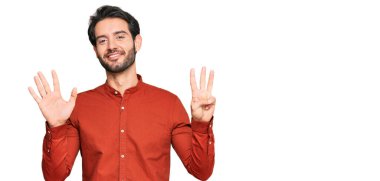 Gündelik kıyafetler giyen genç İspanyol adam sekiz numarayı gösterip işaret ederken kendinden emin ve mutlu bir şekilde gülümsüyor.. 