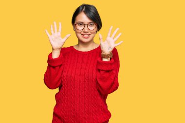 Kısa saçlı, sıradan bir süveter giyen, gözlüklü, on numaralı parmaklarıyla onu gösteren, kendinden emin ve mutlu gülümseyen güzel İspanyol bir kadın.. 