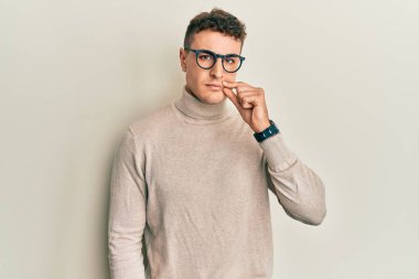 Balıkçı yaka kazak giyen İspanyol genç adam ağzı ve dudakları parmaklarıyla fermuar gibi kapalı. gizli ve sessiz, tabu konuşması 