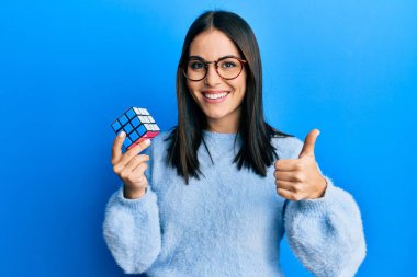 Genç esmer kadın renkli bulmaca oyunu oynuyor mutlu ve pozitif gülümsüyor, başparmağıyla mükemmel ve onay işareti yapıyor. 