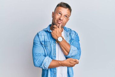 Yakışıklı, sıradan kot ceket giyen, elleri çenesinde soru soran, düşünceli bir adam. Düşünceli bir yüzle gülümsüyor. şüphe kavramı. 