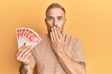 Kafkasyalı genç adam elinde 20 İsrail şekeri olan ağzı elle kapatan banknotlar, şok olmuş ve hata yapmaktan korkan. şaşırmış ifade 