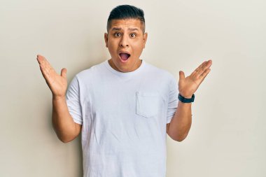 Gündelik beyaz tişört giyen genç latin adam çılgınlığı kutluyor ve başarıya hayret ediyor kolları açık ve gözleri açık heyecanla haykırıyor. Kazanan konsept 