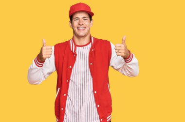 Beyzbol üniforması giyen yakışıklı beyaz adam elinde olumlu bir jest yapıyor, gülümsüyor ve mutlu. Neşeli ifade ve kazanan jest. 