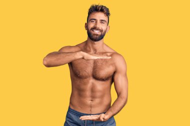 Mayo giyen, büyük ve büyük beden işareti gösteren, mayosuz el kol hareketi yapan genç İspanyol bir adam. Kameraya bakıp gülümsüyor. ölçüm kavramı. 