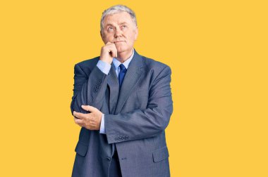 Yaşlı, gri saçlı, iş ceketi giyen, çenesi üstünde soru soran, düşünceli bir adam. Gülümseyen ve düşünceli bir yüz. şüphe kavramı. 