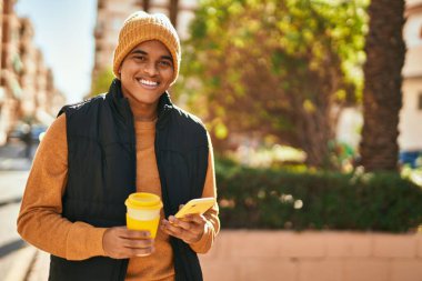 Genç Latin adam akıllı telefon kullanıyor ve şehirde kahve içiyor.