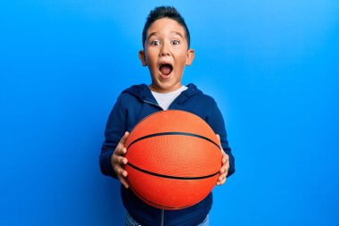 Küçük İspanyol çocuk basketbol topu tutuyor. Çılgınlığı kutluyor ve başarıya hayret ediyor. Gözleri açık, heyecanlı bir şekilde bağırıyor.. 