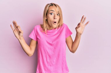 Gayri resmi pembe tişört giyen güzel sarışın kadın şaşırmış ve şok olmuş bir şekilde parmaklarıyla onay sembolü yapıyor. çılgın ifade 