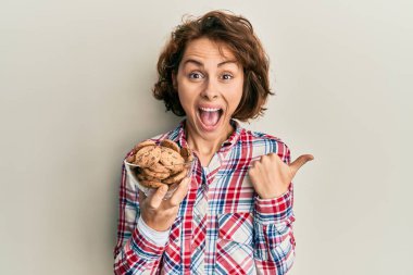 Çikolata parçalı kurabiyeler taşıyan genç esmer kadın başparmağını yana kaldırıyor ve ağzı açık gülümsüyor. 