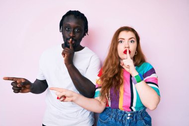 Irklar arası çift günlük kıyafetler giyip sessiz olmak istiyorlar. Parmakları dudaklarında, elleri yandan işaret ediyorlar. sessizlik ve gizli konsept. 