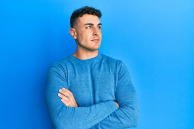 Sıradan bir kazak giyen İspanyol genç adam kollarını kavuşturmuş, ikna olmuş ve kendinden emin bir şekilde yana bakıyor. 