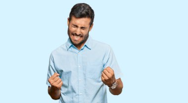 Yakışıklı İspanyol adam gündelik kıyafetler giyiyor. Çok mutlu ve heyecanlı. Kolları havada, gülümseyen ve başarı için bağıran kazanan bir jest yapıyor. kutlama konsepti. 