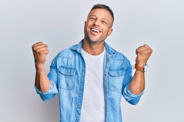 Sıradan kot ceket giyen yakışıklı kaslı adam kolları açık ve gözleri açık bir şekilde başarıyı kutluyor ve şaşırıyor. Kazanan konsept. 