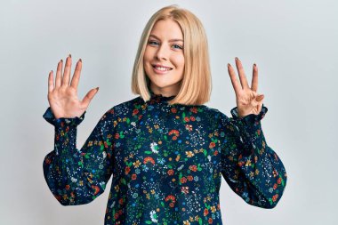 Gündelik kıyafetler giyen genç sarışın kadın sekiz numarayı gösterip işaret ederken kendinden emin ve mutlu bir şekilde gülümsüyor.. 