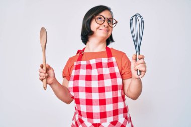 Esmer kadın, aşçı, fırça ve kaşık kullanarak yemek pişiriyor. Gülümsüyor, yan tarafa bakıyor ve düşünüyor.. 