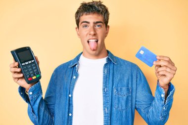 Elinde kredi kartı ve datafon tutan genç yakışıklı adam komik bir ifadeyle mutlu bir şekilde dilini dışarı çıkarıyor.. 