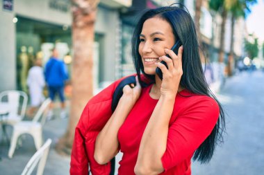 Genç Latin kadın gülümsüyor. Şehirdeki akıllı telefondan konuşuyor..