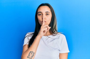 Gündelik beyaz tişört giyen genç İspanyol kadın parmakları dudaklarında sessiz olmak istiyor. sessizlik ve gizli konsept. 