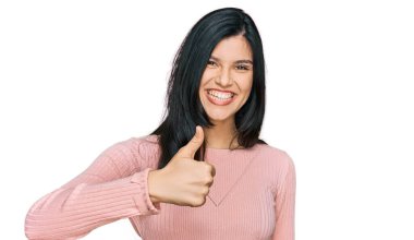 Gündelik kıyafetler giyen genç İspanyol kadın elleriyle mutlu bir jest yapıyor. Kameraya bakıp başarıyı gösteren ifade. 