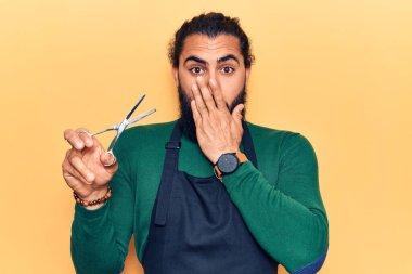 Genç Arap adam berber önlüğü takıyor. Ağzını eliyle kapatıyor. Şok geçiriyor ve hata yapmaktan korkuyor. şaşırmış ifade 