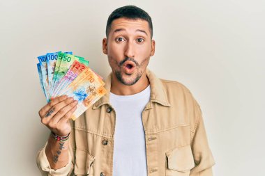Dövmeleri olan yakışıklı bir adam İsviçre frangı banknotları tutuyor. Şaşırtıcı bir şekilde ağzı açık ve korkmuş, inançsız bir yüz. 