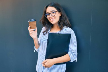 Latin kökenli genç bir iş kadını şehirde kahve içip duruyor.