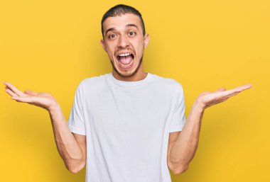 Latin kökenli beyaz tişört giyen genç adam çılgınlığı kutluyor ve başarıya hayran kalıyor kolları açık ve gözleri açık heyecanla bağırıyor. Kazanan konsept 