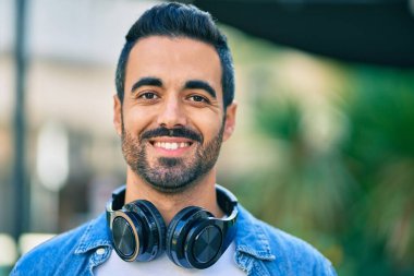 Şehirde kulaklık takarak mutlu gülümseyen genç İspanyol adam..