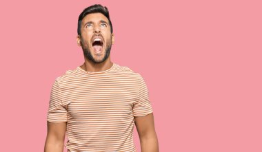 Yakışıklı İspanyol bir adam, gündelik giysiler giyiyor kızgın ve kızgın bağırıyor sinirli ve öfkeli, öfkeyle bağırıyor. öfke ve agresif konsept. 