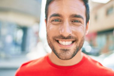 Genç yakışıklı İspanyol adam mutlu gülümsüyor. Yüzünde gülümsemeyle kasaba caddesinde yürürken.