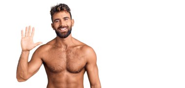 İspanyol asıllı genç adam mayo giyer ve beş numarayı göstererek gülümserken kendinden emin ve mutludur.. 